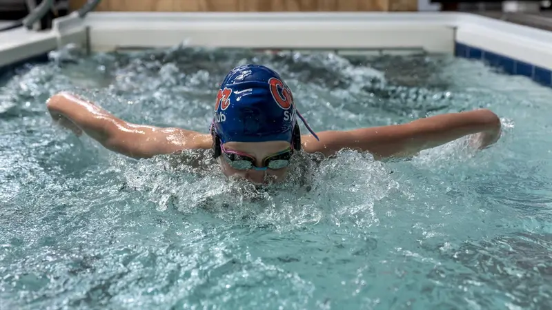 A competitive swimmer swims butterfly toward the camera in the Endless Pool