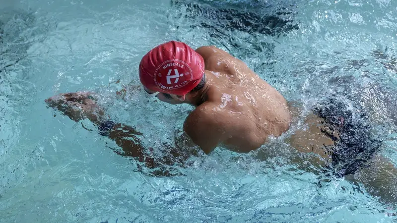 A swimmer in a red cap swims freestyle against the current, seen from above