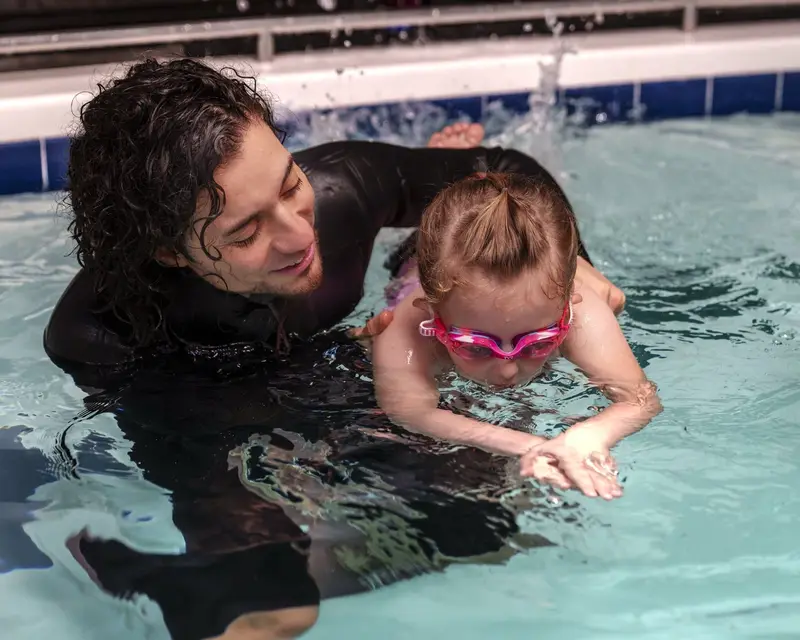 A coach supports a young swimmer’s front crawl during a private lesson