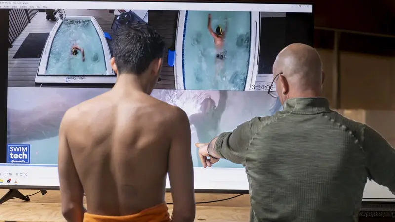 A SwimTec coach points to a frame on the four-camera screen while the swimmer watches